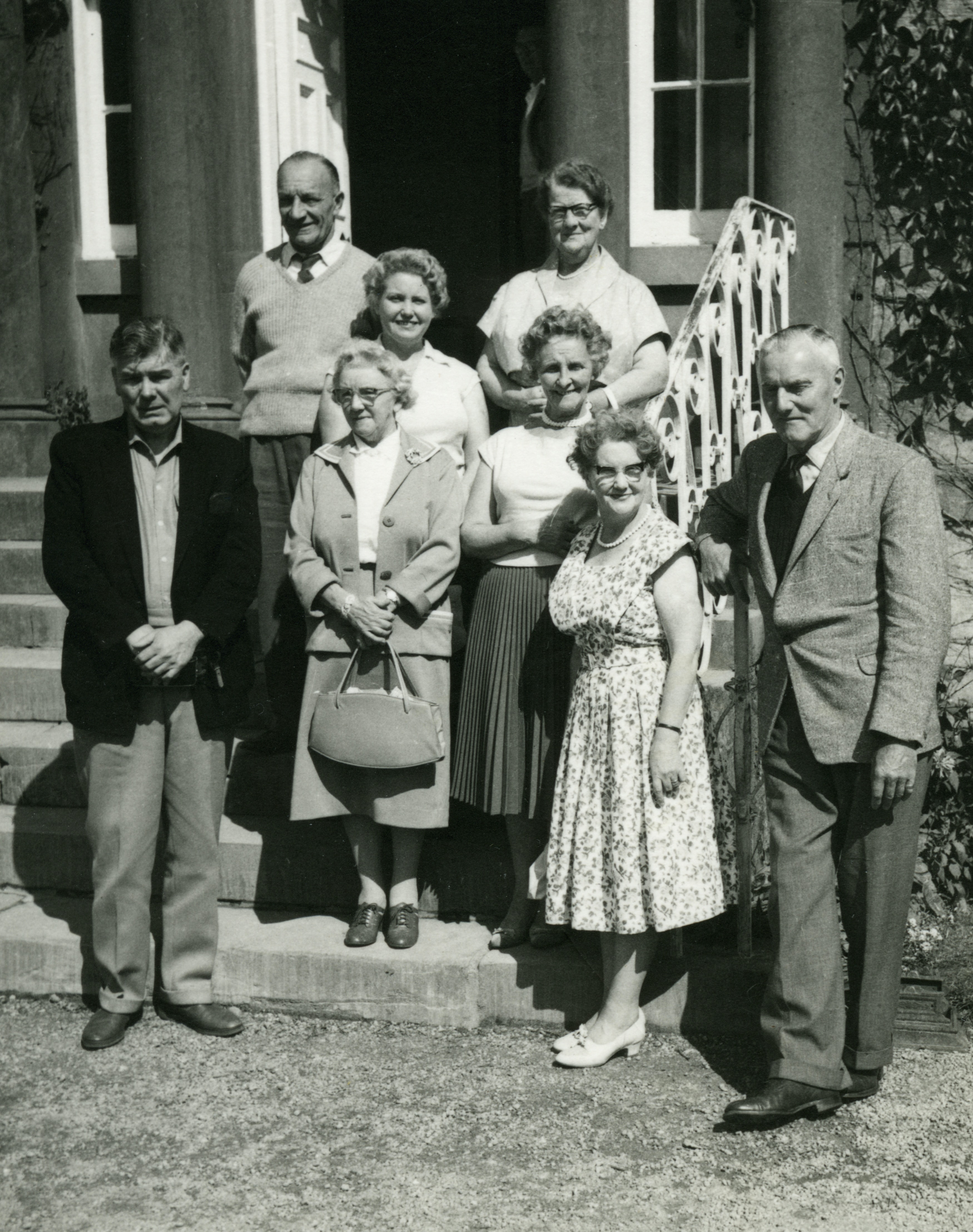 1950s black and white family portrait of 8 people on outside stairs in front of house