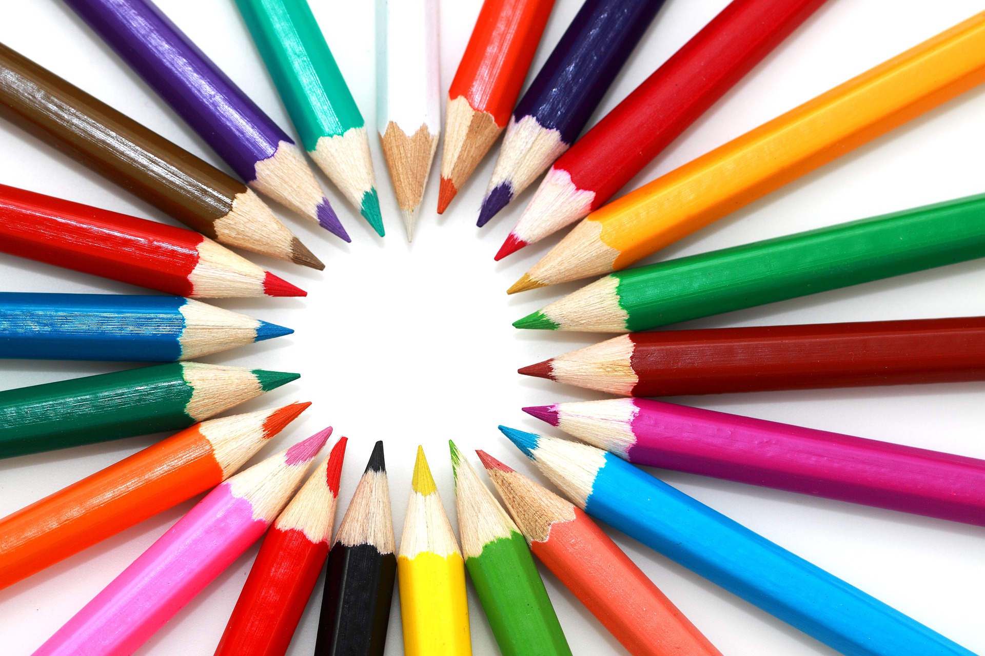 different colored sharpened pencils laid in a circle on white background