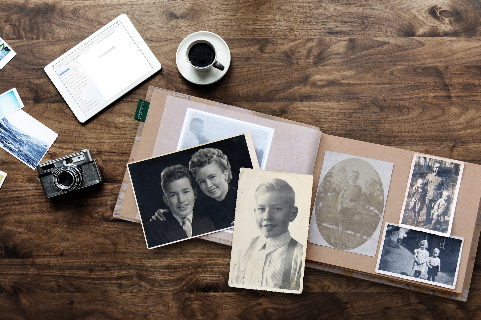 Old photo album, cup of coffee, iPad, and manual camera on wooden table
