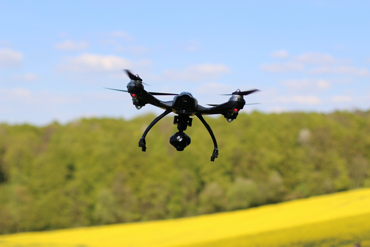 Camera drone flying above a field and trees