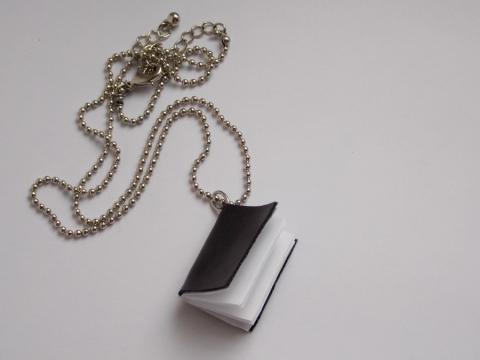 The picture shows a sample of the craft- a miniature black book with white blank pages with silver chain attached at the corner.