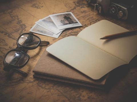 An open notebook and a pair of glasses are on a table.