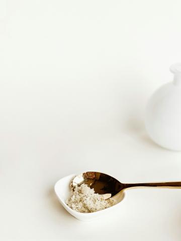 A small white bowl containing a sugar scrub and a golden spoon.