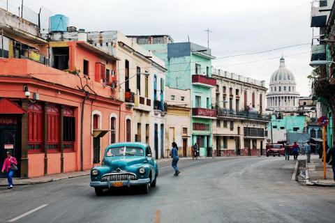 classic car driving down Cuban street with colorful buildings