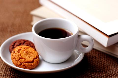 Cup of coffee and two cookies. Books are shown in the background. 