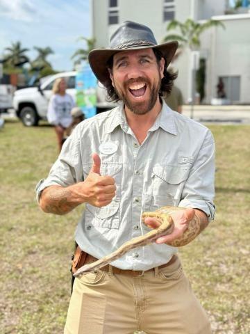 Ranger Rob smiling while holding a snake in one hand and giving a thumbs up with the other hand.