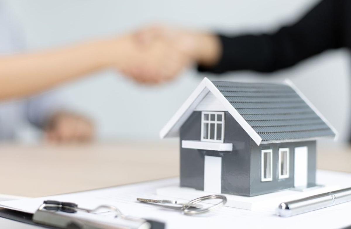 A miniature home in front of two people shaking hands