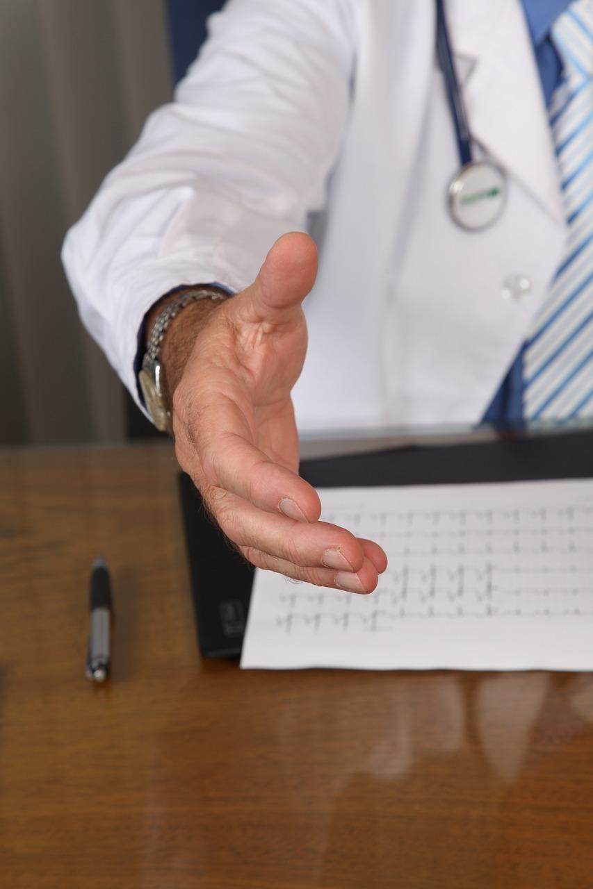 Man in doctor's coat and stethoscope extends hand