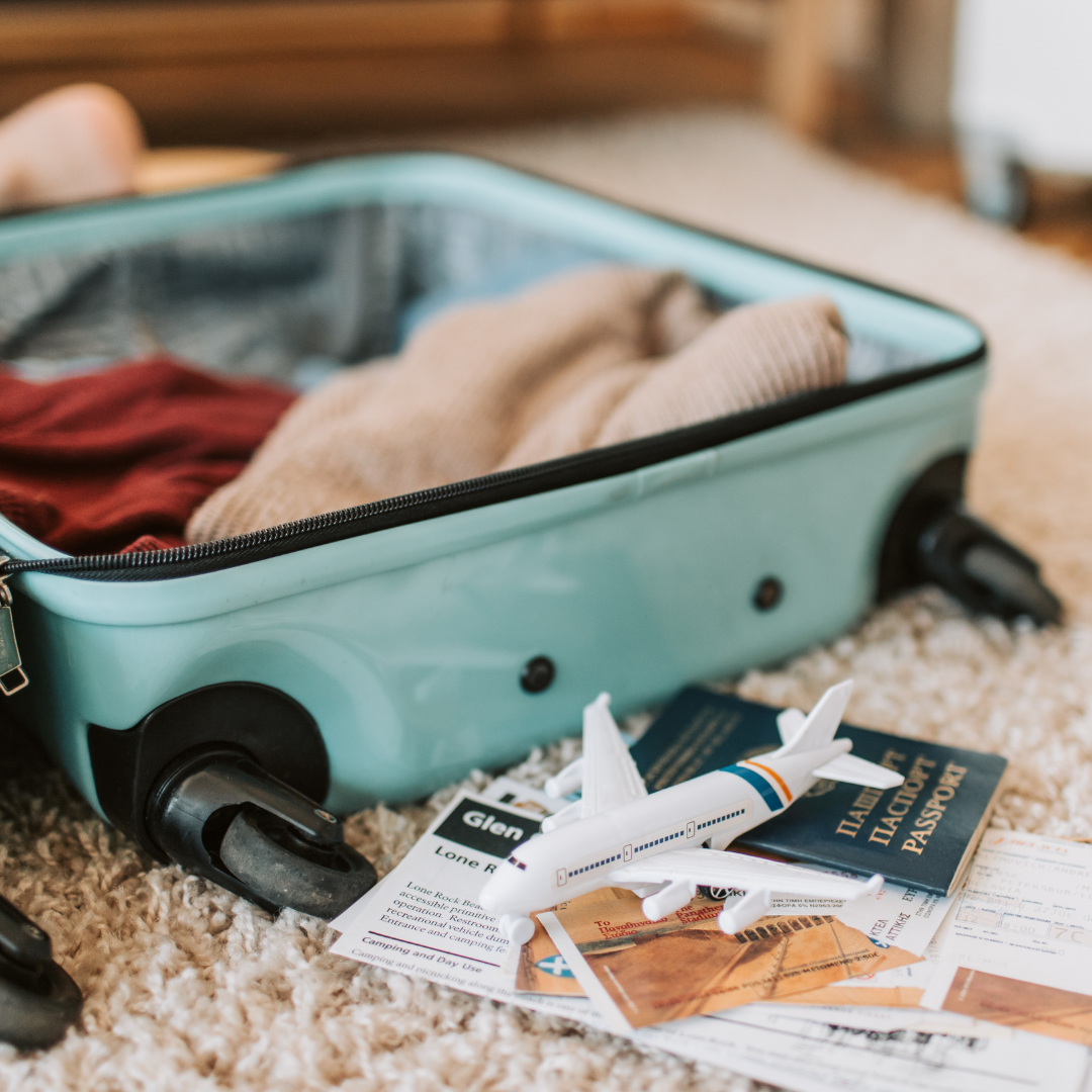 A turquoise suitcase with clothes inside. Next to the suitcase is a passport and a tiny plane. 